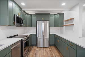 Kitchen featuring light wood finished floors, stainless steel appliances, green cabinetry, and light countertops