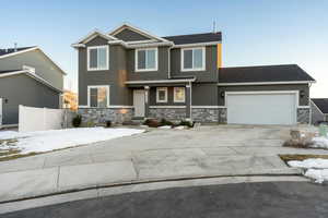 View of front facade featuring concrete driveway, stone siding, an attached garage, fence, and stucco siding