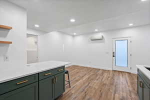 Kitchen featuring a wall unit AC, light countertops, light wood-style floors, green cabinets, and recessed lighting