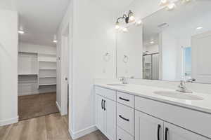 Full bath with double vanity, a spacious closet, a sink, and wood finished floors