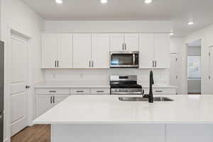 Kitchen featuring appliances with stainless steel finishes, light countertops, light wood-style floors, white cabinetry, and a sink