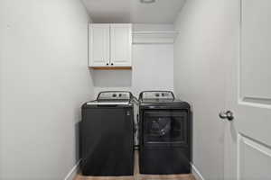 Clothes washing area with cabinet space, independent washer and dryer, baseboards, and wood finished floors