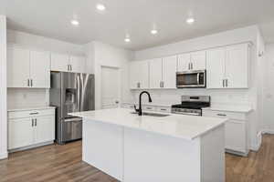 Kitchen featuring wood finished floors, appliances with stainless steel finishes, a sink, and white cabinets