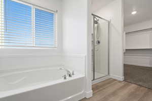 Bathroom featuring a walk in closet, a garden tub, a shower stall, and wood finished floors