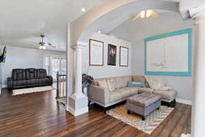 Living room with ceiling fan, dark wood-style floors, and ornate columns