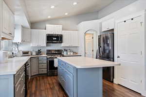 Kitchen featuring stainless steel appliances, a sink, white cabinets, light countertops, and a center island