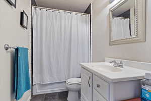 Bathroom featuring toilet, a textured ceiling, vanity, and shower / tub combo with curtain