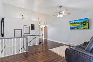 Living room with arched walkways, visible vents, dark wood-type flooring, vaulted ceiling, and baseboards