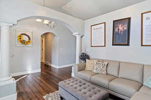 Living room featuring arched walkways, baseboards, vaulted ceiling, dark wood-style floors, and decorative columns