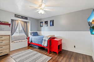 Bedroom with a ceiling fan, wainscoting, dark wood finished floors, and a textured ceiling