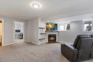 Living area with baseboards, visible vents, light colored carpet, a fireplace with flush hearth, and a textured ceiling