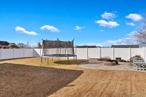 View of yard featuring an outdoor fire pit, a fenced backyard, and a trampoline