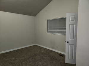 Spare room featuring lofted ceiling, baseboards, dark colored carpet, and a textured ceiling