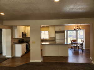 Kitchen featuring a center island, dark wood-style flooring, an inviting chandelier, appliances with stainless steel finishes, and white cabinetry