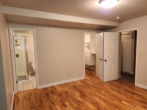 Unfurnished bedroom with light wood finished floors, baseboards, a textured ceiling, and ensuite bathroom