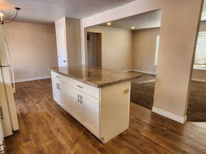 Kitchen featuring light stone counters, dark wood-style flooring, white cabinetry, freestanding refrigerator, and a center island