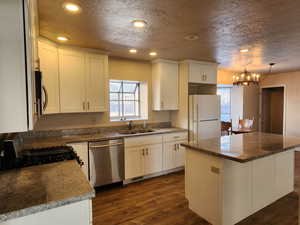 Kitchen featuring dark wood finished floors, stainless steel appliances, white cabinets, a kitchen island, and a sink