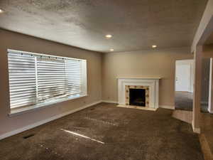 Unfurnished living room featuring dark carpet, a high end fireplace, visible vents, and baseboards