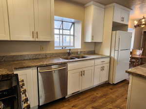 Kitchen with a sink, white cabinets, freestanding refrigerator, dishwasher, and dark countertops