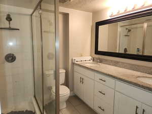 Full bath featuring double vanity, toilet, a stall shower, a sink, and a textured ceiling