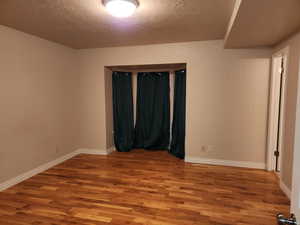 Empty room with a textured ceiling, baseboards, and wood finished floors