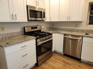 Kitchen with light wood-style flooring, white cabinetry, stainless steel appliances, and light countertops