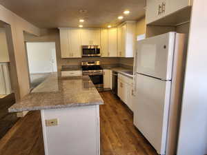 Kitchen with light stone counters, recessed lighting, white cabinetry, appliances with stainless steel finishes, and dark wood finished floors