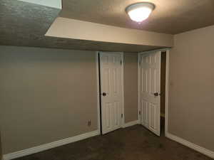 Below grade area with dark carpet, a textured ceiling, and baseboards