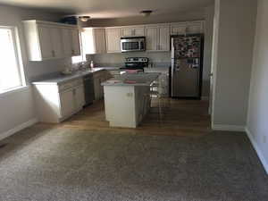 Kitchen featuring light countertops, appliances with stainless steel finishes, a kitchen island, a sink, and a kitchen breakfast bar