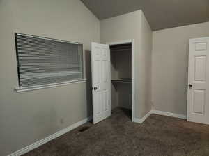 Unfurnished bedroom with a closet, dark carpet, visible vents, and baseboards