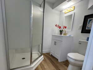 Bathroom featuring toilet, hardwood / wood-style flooring, visible vents, vanity, and a shower stall