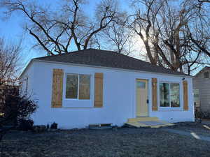 Bungalow-style home with a shingled roof, a front lawn, and stucco siding