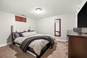 Bedroom with light colored carpet, visible vents, baseboards, and a textured ceiling