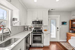 Kitchen featuring appliances with stainless steel finishes, white cabinetry, a sink, and tasteful backsplash