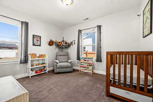 Carpeted bedroom featuring baseboards, visible vents, a crib, and a textured ceiling