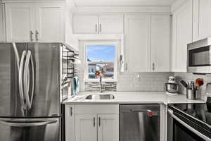 Kitchen with stainless steel appliances, a sink, white cabinetry, light countertops, and tasteful backsplash