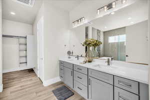 Full bath featuring a walk in shower, double vanity, a sink, and wood finished floors