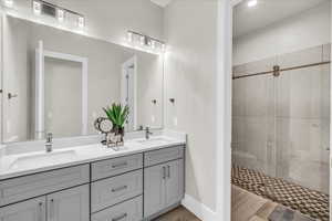 Bathroom with double vanity, a shower stall, a sink, and wood finished floors