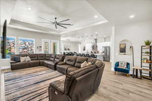 Living room with light wood finished floors, ceiling fan, baseboards, and a raised ceiling