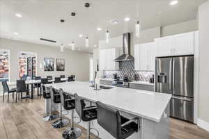 Kitchen with stainless steel appliances, visible vents, decorative backsplash, an island with sink, and wall chimney exhaust hood