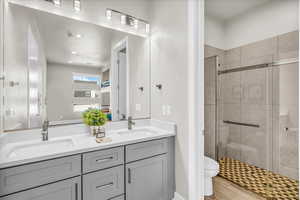 Bathroom featuring a sink, a shower stall, toilet, and double vanity