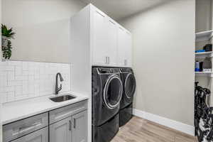 Clothes washing area featuring cabinet space, baseboards, light wood-style flooring, washing machine and clothes dryer, and a sink