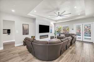 Living room with baseboards, light wood-style flooring, ceiling fan, a tray ceiling, and a fireplace