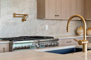 Room details with light countertops, backsplash, light brown cabinetry, modern cabinets, and range