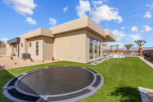 Rear view of house with central AC, a trampoline, a lawn, and stucco siding