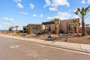 Pueblo-style home with stone siding, driveway, an attached garage, and stucco siding