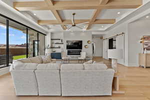 Living area with a barn door, beam ceiling, coffered ceiling, and a ceiling fan