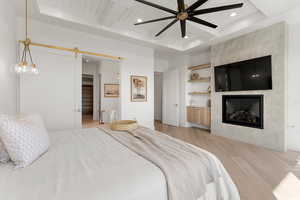 Bedroom with a barn door, light wood-style floors, a fireplace, beam ceiling, and recessed lighting