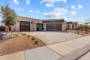 View of front facade with a garage, stone siding, concrete driveway, and stucco siding