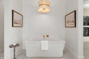 Bathroom with a freestanding bath, marble finish floor, and baseboards